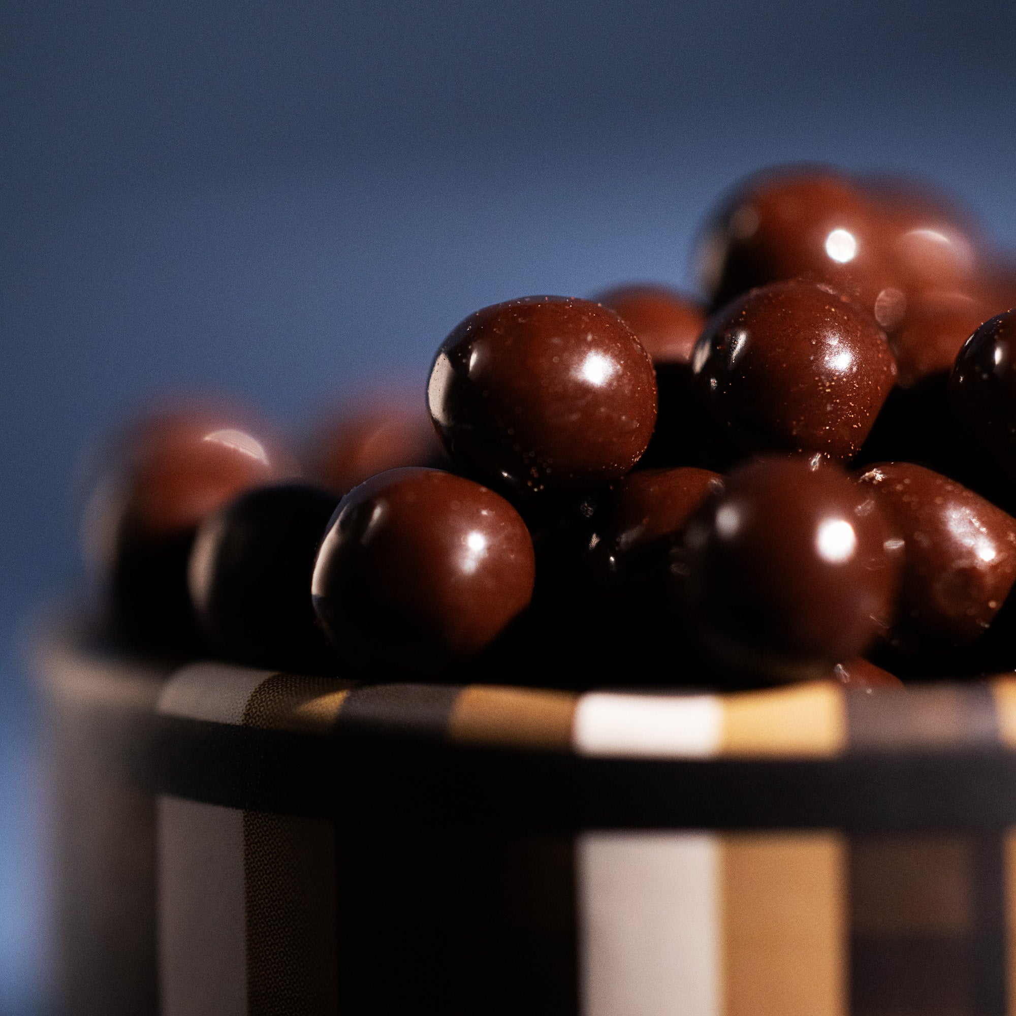 Close-up of chocolate-covered coffee pearls in a striped container with a blue background