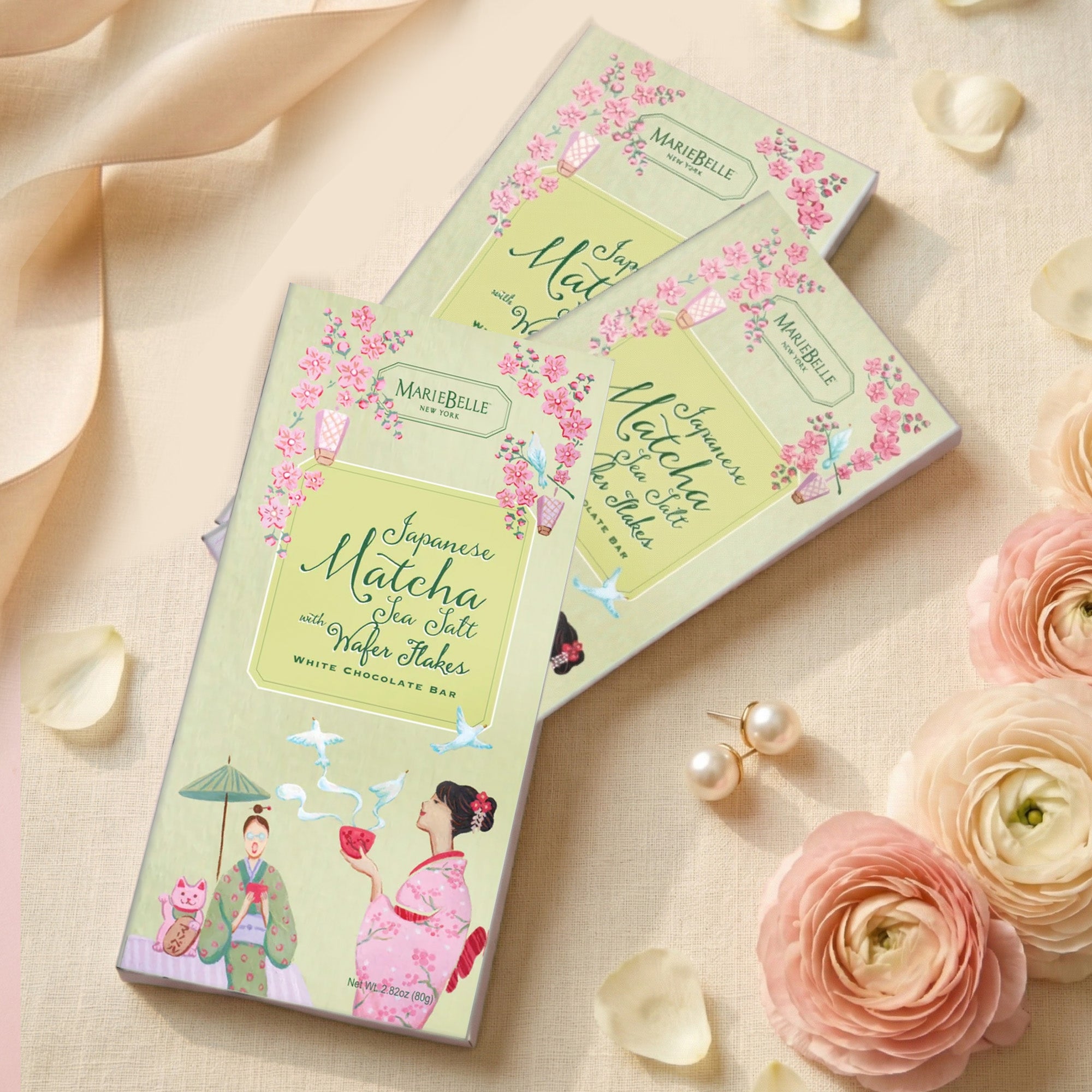 MarieBelle Chocolate bars with decorative packaging on a soft background with flowers and jewelry.